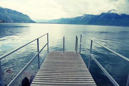 Old wooden pier with railing in rainy day on Lake Geneva, Montreux, Switzerland. Toned imageの写真素材