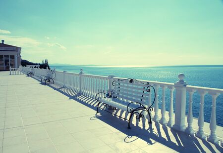 Summer view with classic white balustrade, benches and empty terrace overlooking the sea, sunlight. Vintage toned imageの写真素材