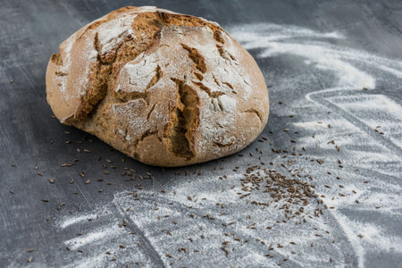 Fresh homemade caraway bread with sunflower seeds on a gray background with spilled flour