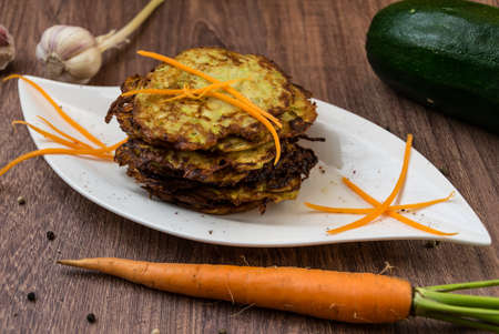 Fried zucchini with herbs and garlic on white plate decorated with grated carrotの写真素材