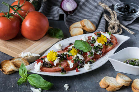Fresh refreshing salad of mozzarella and red tomatoes on white plate. Spilled with olive oil with pieces of black olives, basil and red onionsの写真素材