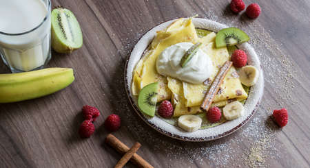 Homemade pancake with vanilla curd, raspberries, kiwi and banana pieces sprinkled with cocoaの写真素材