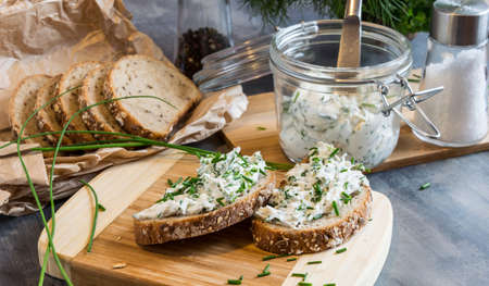 Home made bread on a wooden cutting board with curd cheese and ricotta and herbs. Decorated with green herbsの写真素材
