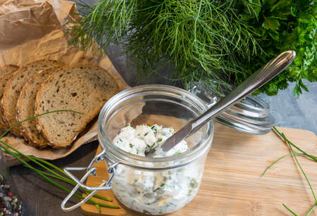 Home made bread on a wooden cutting board with curd cheese and ricotta and herbs. Decorated with green herbsの写真素材