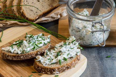 Home made bread on a wooden cutting board with curd cheese and ricotta and herbs. Decorated with green herbsの写真素材