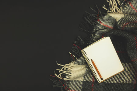 Workplace design with a plaid and a notebook, black background, minimalism, copy space, top view photoの写真素材