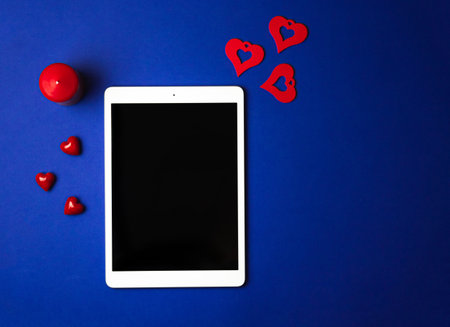 Tempalate tablet with Valentine's Day decorations on form of heart, love red candle on blue background, top view. High quality photoの写真素材