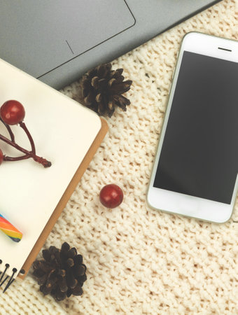 Flat lay winter composition, cozy background with smartphone, workplace or workspace at holiday, pine cones on knitted sweater photoの写真素材