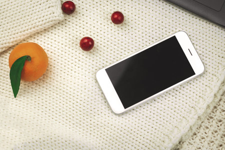 Winter cozy composition, tangerines, decoration and smartphone on blachround of kniteed warm sweaters, copy space photoの写真素材