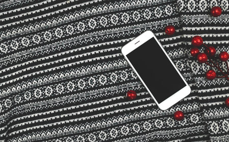 Knitted sweater background with red decoration, blank white smartphone, copy space cozy banner. High quality photoの写真素材