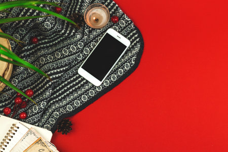 Flat lay cozy composition with knitted red background, smartphone, candle and decorations, hygge concept, copy space photoの写真素材