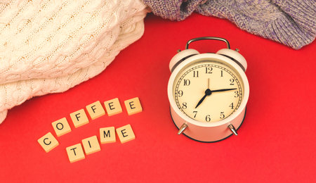 Coffee time morning concept, old vintage alarm clock on red retro background, knitted sweaters photoの写真素材
