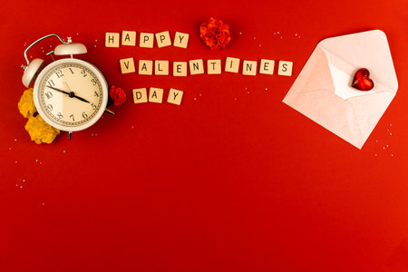 Valentine's day greeting card concept, red background, envelop and morning alarm clock, flowers, love red hearts theme, word on cubes, photoの写真素材