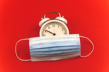COVID-19 concept, new morning composition, wear mask before going outside, alarm clock and time composition on red background, photoの写真素材