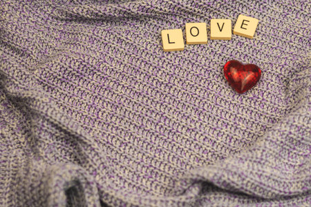 Romantic couple Valentine's Day background on warm knitted cozy sweater, love word and one red heart...