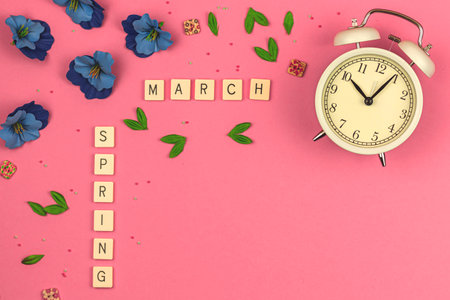 March beauty flat lay concept or background on a vibrant pink, decorative flowers, alarm clock and accessories, copy space photoの写真素材