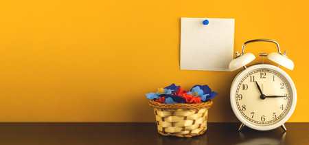 Minimal workspace conceptual creative photo with pinned blank notepad paper, banner with alar clock on a table, yellow background photoの写真素材