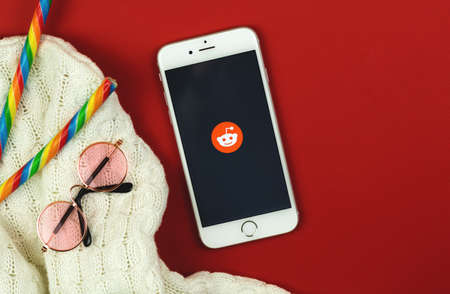 Kharkov, Ukraine - February 22, 2021: creative background with Reddit app logo on Apple smartphone, flat lay workspace, copy space photoのeditorial素材