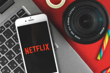 Kharkov, Ukraine - February 22, 2021: Netflix logo on smartphone Apple, mobile application of streaming service, flat lay creative composition, red backgroundのeditorial素材