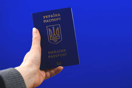 Ukrainian passport in hand, personal document proving the identity of a citizen, blue isolated background photoの写真素材