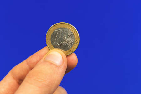 Hand hold one euro coin on a blue isolated background, close-up photoの写真素材