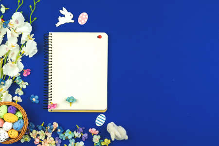 Easter holiday mockup and greeting card concept with blankn white paper, notebook, spring flowers on a blue background, top view photoの写真素材