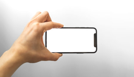 Kharkov, Ukraine - April 3, 2021: Hand horizontally holds Apple iPhone 12, mockup with blank white screenのeditorial素材