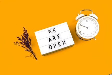 Creative flat lay sign We are open with alarm clock and flowers, top view, business and cafe...