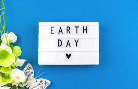 Earth Day flat lay creative background with flowers and text message on a lightbox, blue paper photo