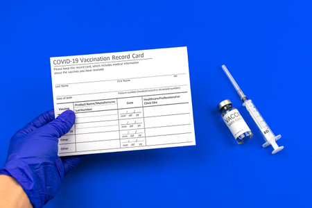 COVID-19 vaccination record card in doctor's hand, immunization concept photo, blue table with...