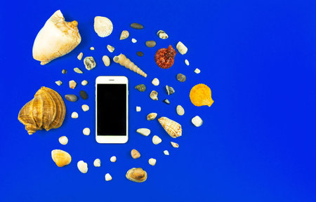 Summer smartphone mockup with seashell and pebbles on a blue background, vacation flat lay...