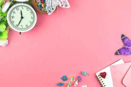 Feminine workspace border composition, flat lay pink background, office desk with flowers, alarm clock and butterflies, copy space photoの写真素材