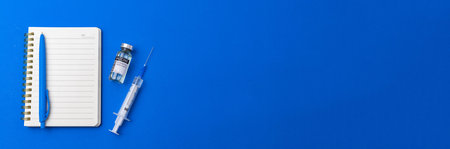 Vaccination banner with blue background, vaccine vial with syringe on a table, notebook with pen,...