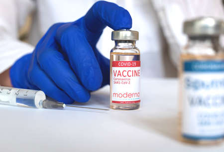 Kharkov, Ukraine - April 19, 2021: Coronavirus vaccination by Moderna vaccine, doctor use glass bottle with vaccine by Americam company, glass table photoのeditorial素材