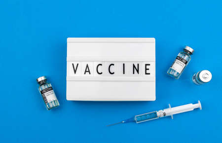Vaccine text background with coronavirus vaccines and medical syringe, lightbox with lettering on blue tableの写真素材