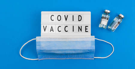 Covid vaccine text message, sign with words, vaccine vials and medical mask on the blue background, vaccination and healthcare conceptの写真素材