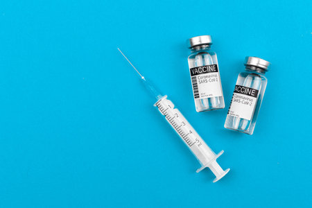 Vials with coronavirus vaccine and syringe on bright background, flat lay and top view