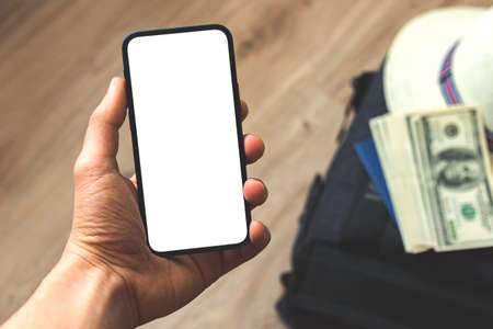 Hand with screen mockup on background of traveler bag, money and straw hat, concept template pf preparation for world triip, copy spaceの写真素材