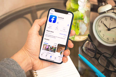 Kharkov, Ukraine - April 27, 2021: Man hold mobile phone with Facebook app store page, social network concept background photoのeditorial素材