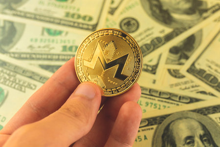 Monero coin in hand on background of dollar bills, trading and exchange concept photo
