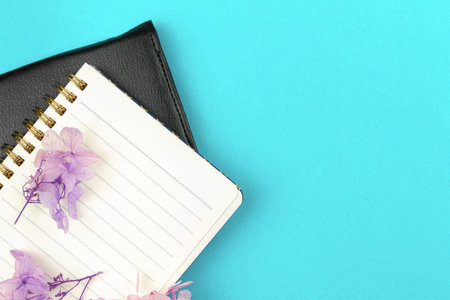 Business diary concept, notebook with purple flowers on bright background, flat lay and copy space