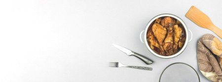 Banner dinner cooking concept, roasted chichen in a saucepan on white and silver background kitchen workspace top view, towel, fork and wooden spoonの写真素材