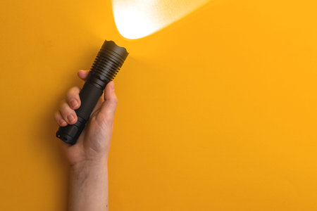 Person use black edc flashlight, office desk yellow background, top view, home equipment concept