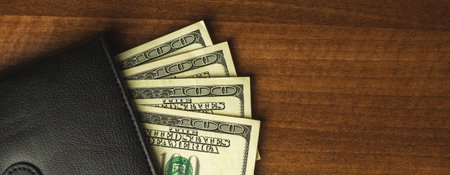 Money in wallet, one hundred US bills in black men's purse, wooden table background, top view and...