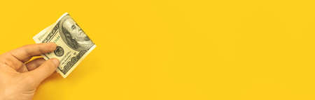 Concept of investment money, man hand with US one hundred dollar bill, yellow office table background, banner with copy space photoの写真素材