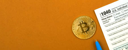 Business office desk with US Individual Income Tax Return form and physical bitcoin coin, top view photo, banner with copy spaceの写真素材