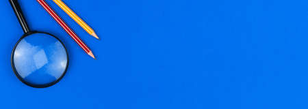 School equipment banner, education concept, blue office desk with magnifying glass and pencils, copy space and top view photoの写真素材