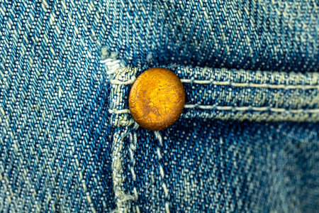 Bronze metal rivet on a blue denim jeans with stitched seam of pocket, close up background