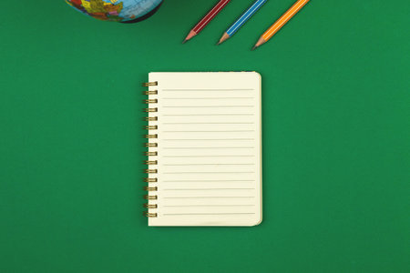 Green school table with blank lined notebook and pencils top view with copy space