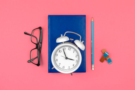 School pink workspace with alarm clock, notebook diary and alarm clock on the table background, top...